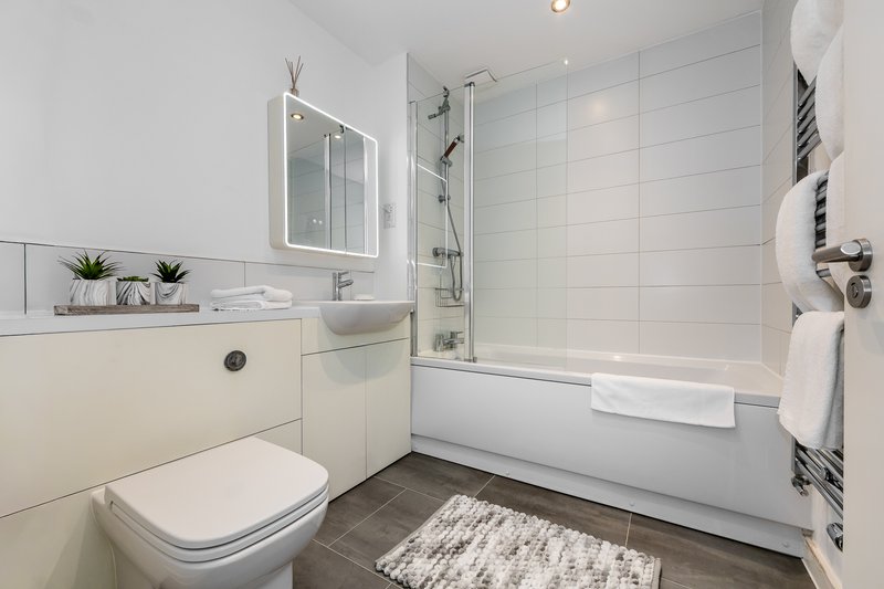 Modern bathroom with toilet, sink, bathtub with shower screen and heated towel rail