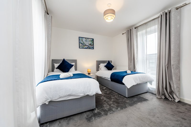 Bright bedroom with two single beds, blue bedding, navy cushions, wooden headboards and curtains
