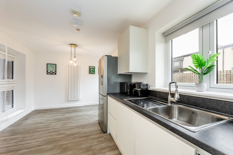 Modern kitchen with cream cabinetry, black countertops, stainless steel sink and appliances