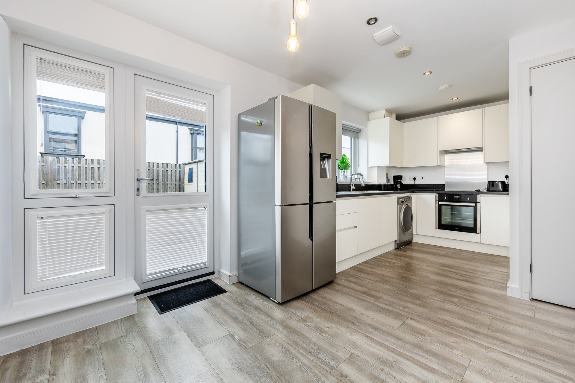 Modern kitchen with white cabinetry, stainless steel appliances, wooden flooring and glass doors to balcony