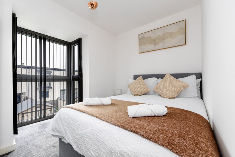 Modern bedroom with double bed, brown throw blanket, cushions, and black balcony doors