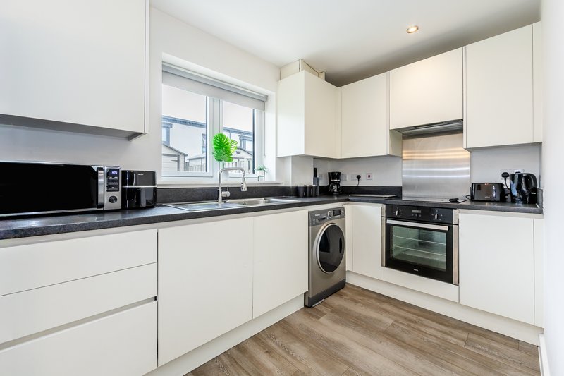 Modern kitchen with white cabinetry, black countertop, integrated appliances and wooden flooring