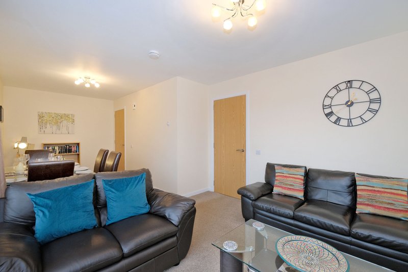Open-plan living room with two black leather sofas, blue cushions, coffee table, and wall clock