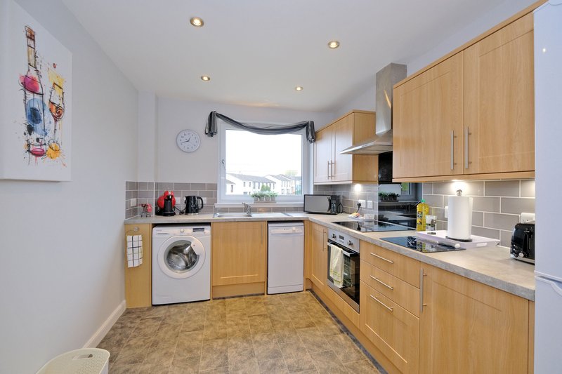 Modern kitchen with wooden cabinets, white appliances, and window overlooking garden