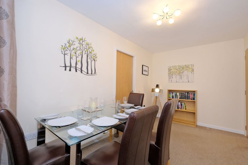 Dining room with glass table, brown chairs, wall art and bookshelf