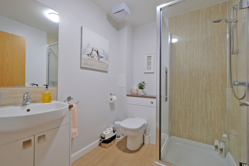 Clean modern bathroom with white sink, toilet, shower enclosure and wooden flooring