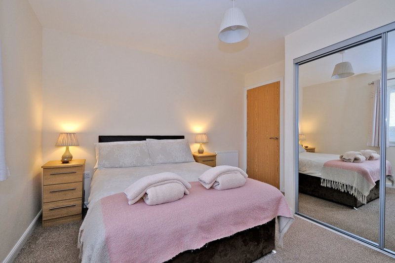 Bright bedroom with double bed, pink throw, bedside tables with lamps, and mirrored wardrobe