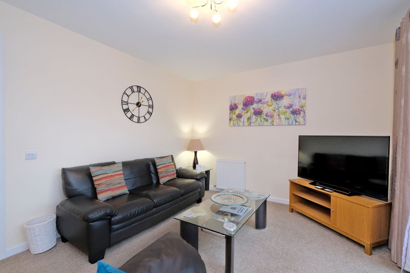 Living room with dark leather sofa, glass coffee table, TV on wooden stand, wall clock and floral artwork