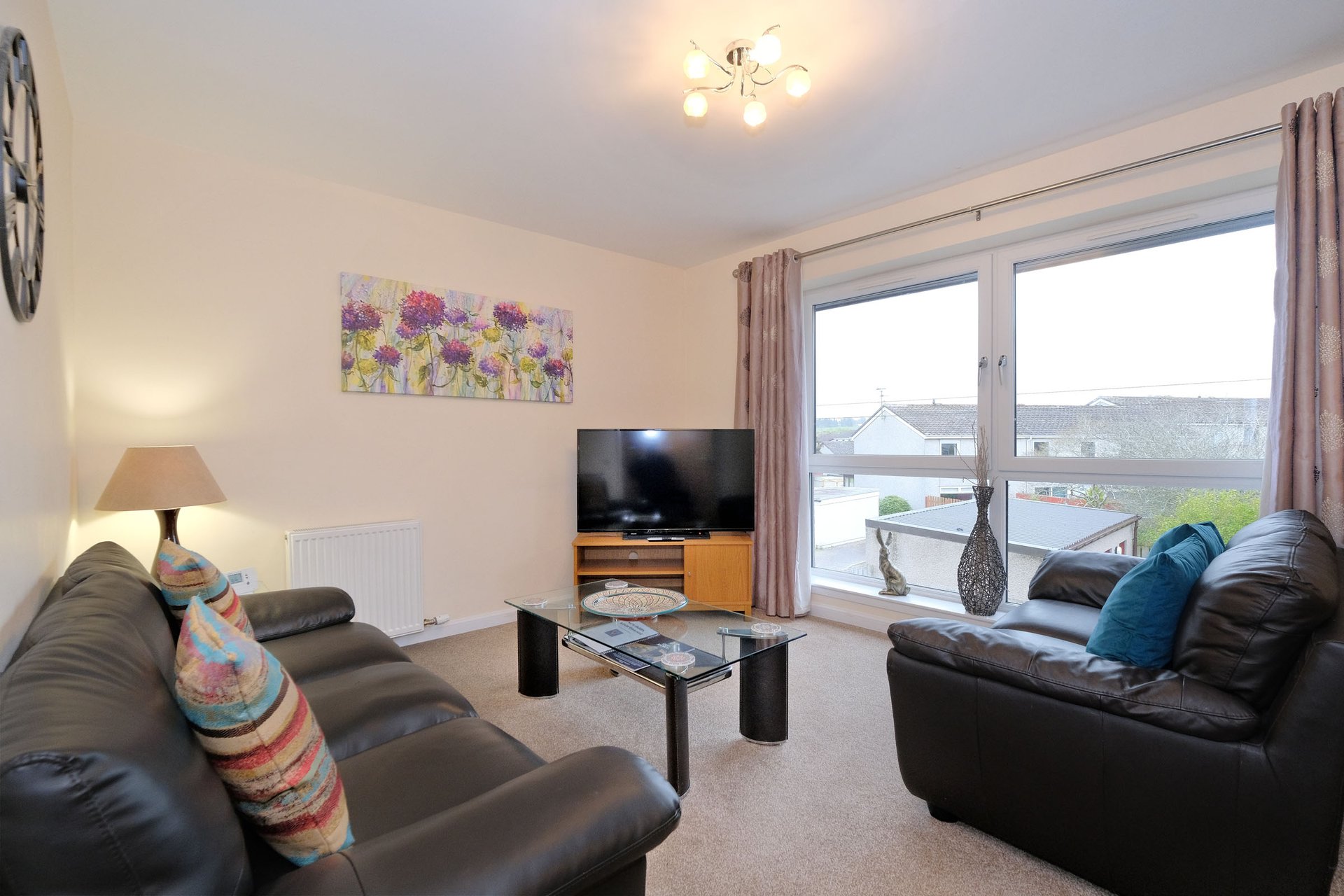 Bright living room with black leather sofas, TV, coffee table and large window overlooking garden