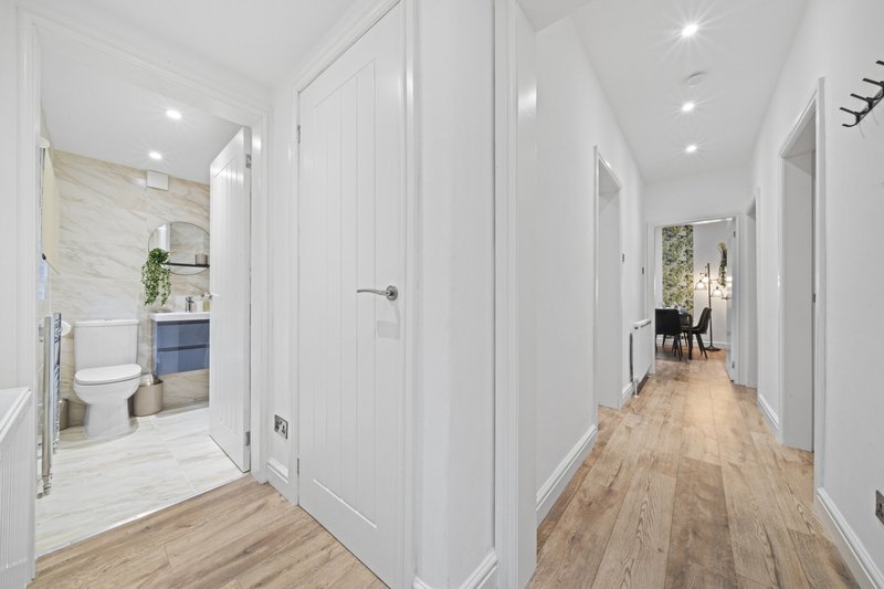 Bright hallway with white panelled doors, wooden flooring, and ensuite bathroom visible on left