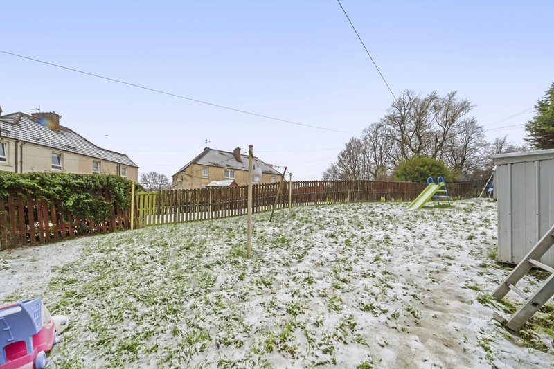 Snowy garden with wooden fencing, neighboring houses and outbuildings visible