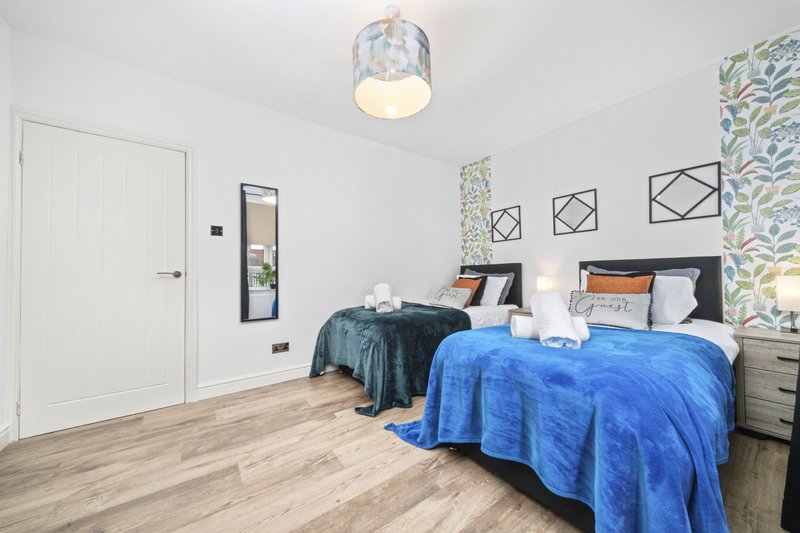 Modern bedroom with two beds, blue bedding, wooden floor and wall decor
