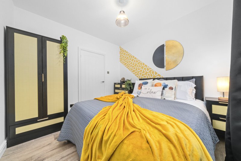 Modern bedroom with double bed, yellow throw, wardrobe and wall art