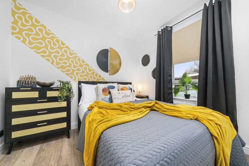 Modern bedroom with yellow and gray bedding, black striped dresser, decorative wall art and pendant lighting