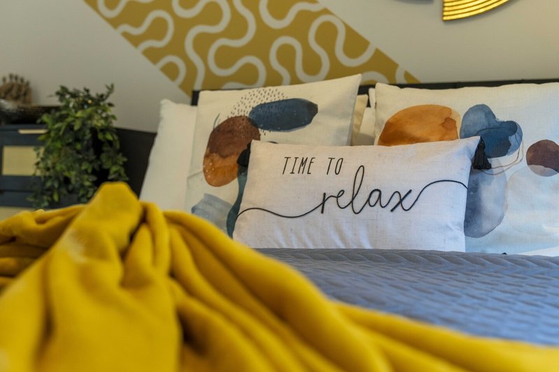 Bedroom with double bed, patterned headboard, decorative pillows and yellow bedding