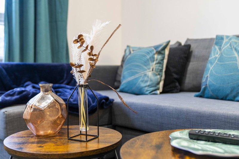 Living room with grey sofa, blue cushions, wooden coffee table with vase and dried flowers