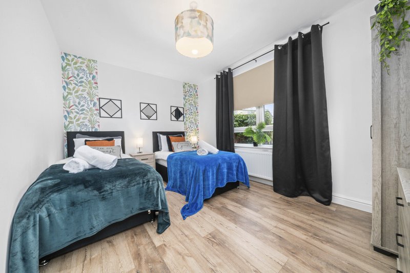 Bright bedroom with two single beds, teal and blue bedding, wooden flooring, and large window with black curtains