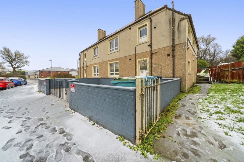 Two-story brick residential building with driveway, fenced garden area, and parked cars