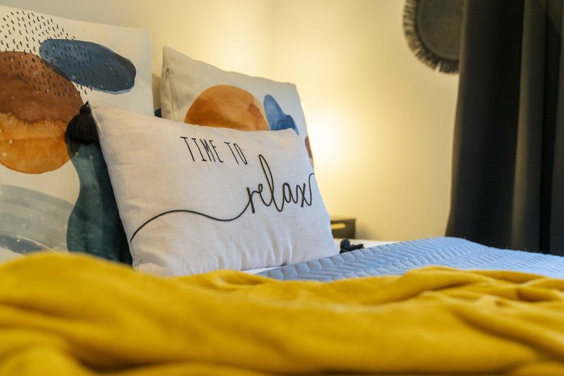 Bedroom with yellow bedding, decorative pillows with geometric patterns and text