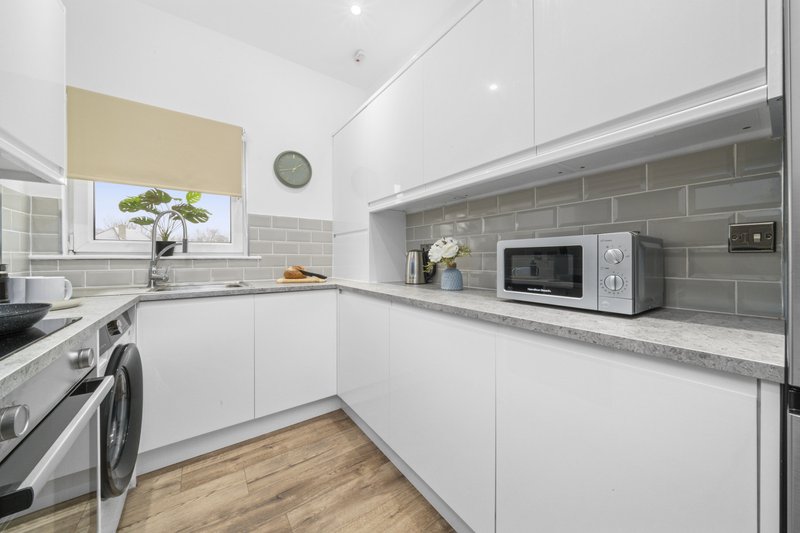 Modern white kitchen with grey subway tile backsplash, stainless steel appliances and wooden floor