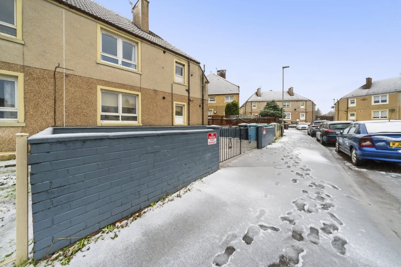Snowy residential street with stone-built houses, blue fence, and parked cars
