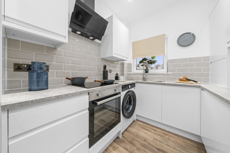 Modern white kitchen with grey subway tile backsplash, integrated appliances and wooden flooring