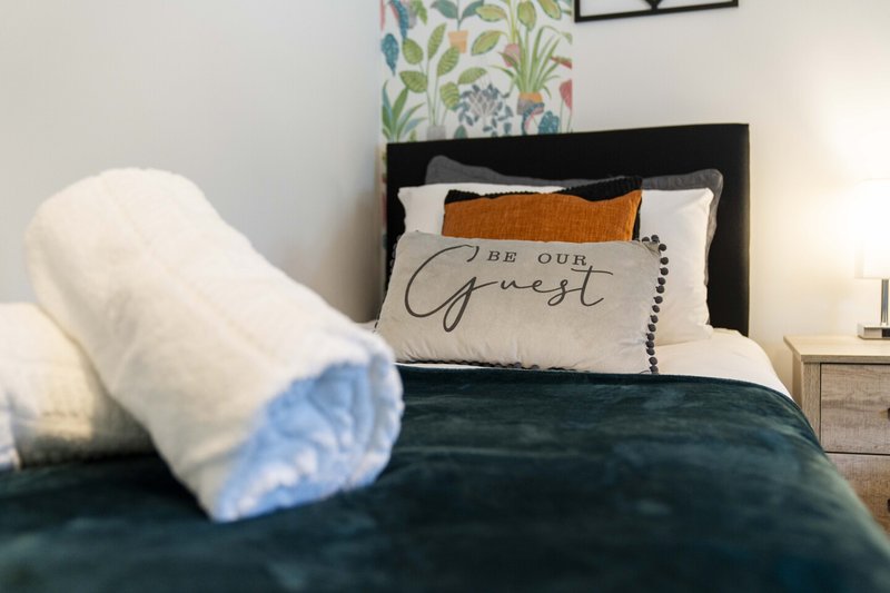 Bedroom with black headboard, green bedding, decorative pillows and white rolled towel