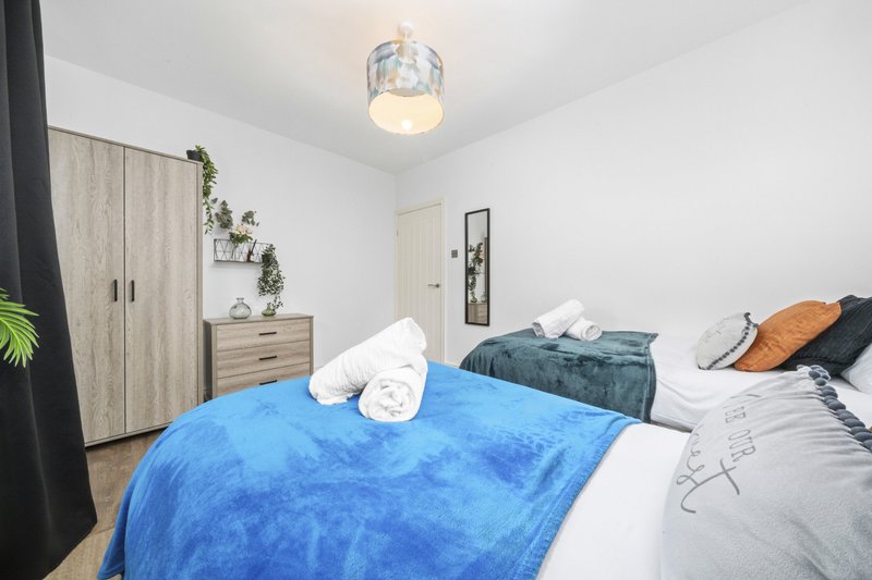 Modern bedroom with two beds, blue throw blanket, wooden furniture and pendant ceiling light