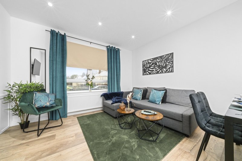 Modern living room with grey sofa, teal curtains, green area rug and wooden flooring