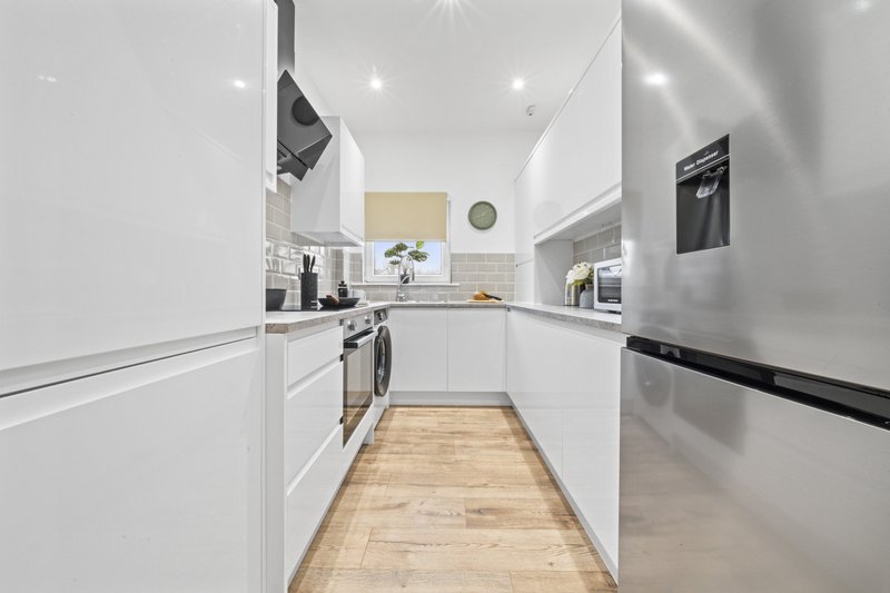 Modern galley kitchen with white cabinetry, wooden flooring, stainless steel appliances and pendant lighting