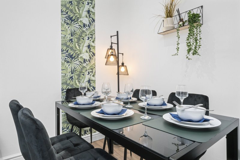 Modern dining room with black table, blue place settings, pendant lighting, and plant decor