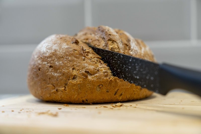 Freshly baked bread loaf with knife on wooden cutting board