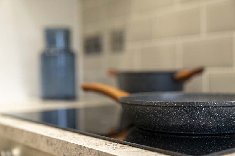Kitchen stovetop with black frying pans and blue bottle, white tile backsplash
