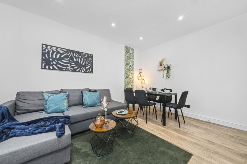 Modern living room with gray sofa, dining table, wooden floor and wall art