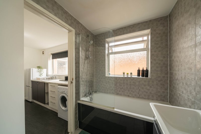 Modern bathroom with bathtub, window, sink, washing machine and grey tiled walls