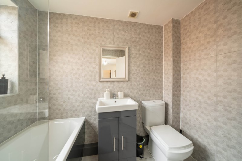 Modern bathroom with bathtub, dark vanity sink, toilet, and tiled walls
