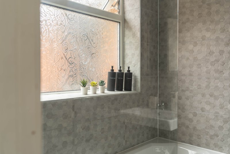 Modern bathroom with grey tile walls, window with frosted film, and bathroom accessories on windowsill