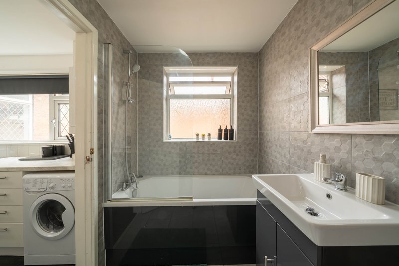 Modern bathroom with bathtub, sink, mirror, washing machine and window