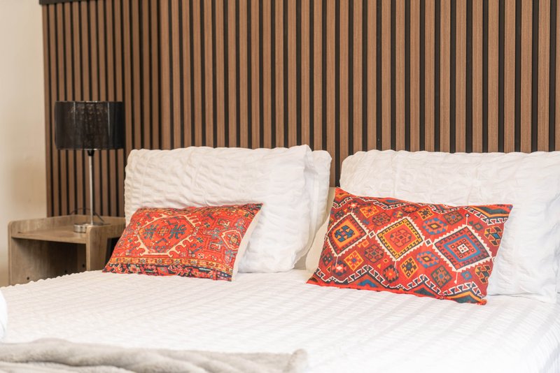 Modern bedroom with double bed, white bedding, patterned orange cushions and wooden slat headboard