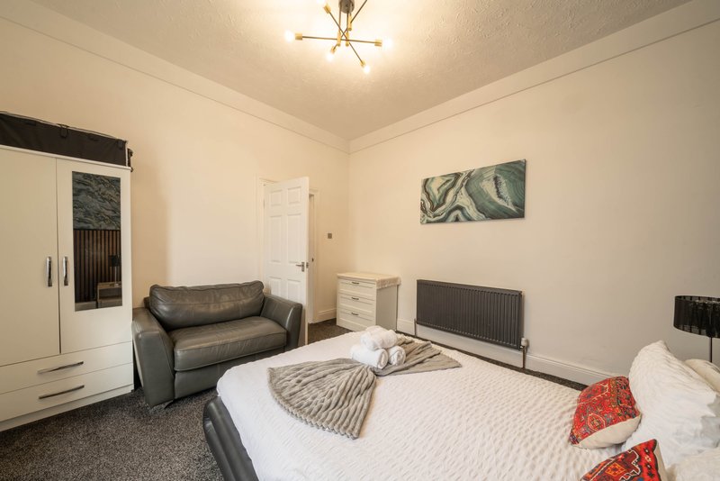 Bedroom with double bed, grey sofa, wardrobe, chest of drawers and radiator