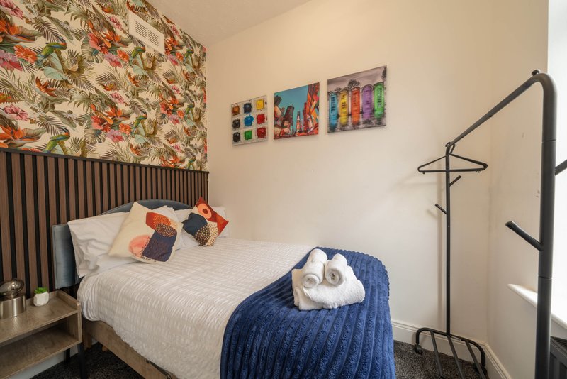 Bedroom with double bed, floral headboard, colorful wall art, and towel rail