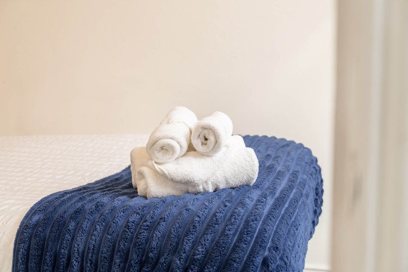 Rolled white towels stacked on blue quilted bedspread against cream wall