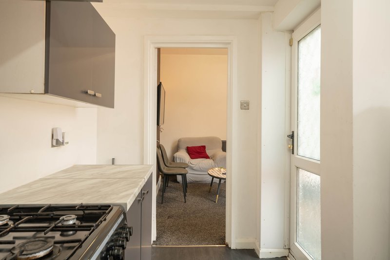 Kitchen with gas hob and grey cabinetry, doorway to living area with seating visible
