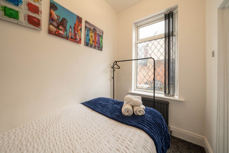 Small bedroom with single bed, metal frame, window, and colorful wall art