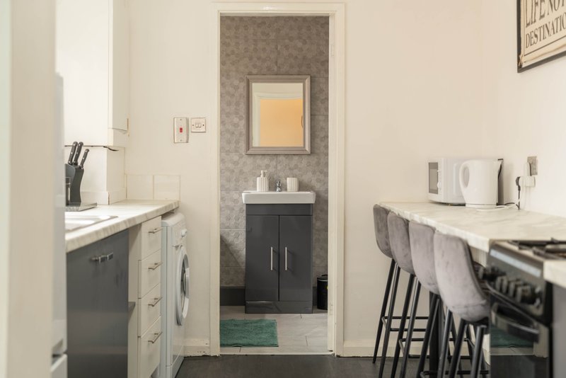Modern kitchen with grey cabinetry, white countertops, washing machine and bar seating area