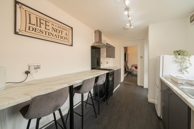 Open-plan kitchen and dining area with wooden counter, black chairs, and wall-mounted inspirational sign
