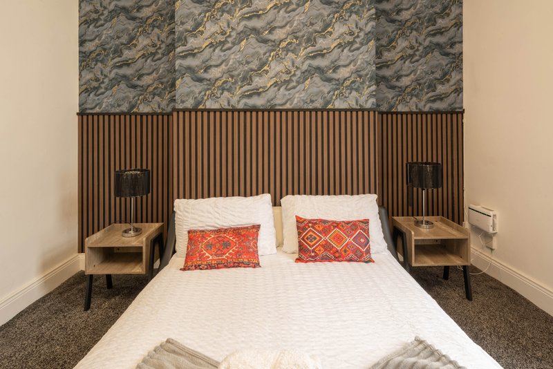 Modern bedroom with double bed, patterned headboard, bedside tables and red cushions