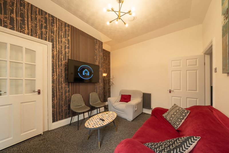 Modern living room with red sofa, accent wall, chairs, and ceiling light fixture