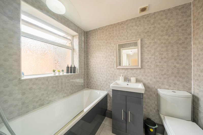Modern bathroom with bathtub, vanity sink, toilet, and window with frosted glass