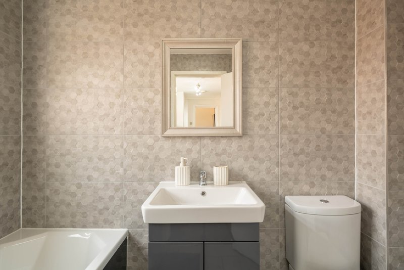 Modern bathroom with white sink, mirror, toilet, bathtub and neutral tile walls